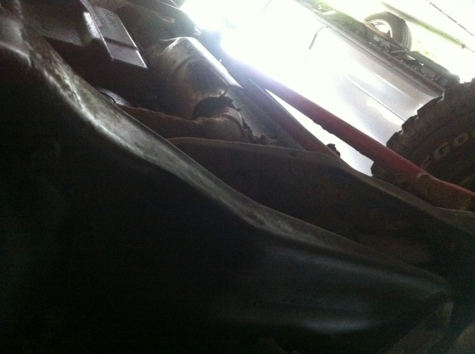 Underside view of vehicle suspension and frame components, with a tire visible in the background