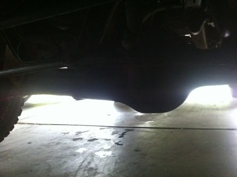 1990 Ford Bronco - The underside of a vehicle shows its rear axle and differential, with some fluid spots on the ground.