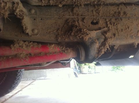 1990 Ford Bronco - The underside of a vehicle is heavily coated in mud, obscuring details of the frame and suspension components.