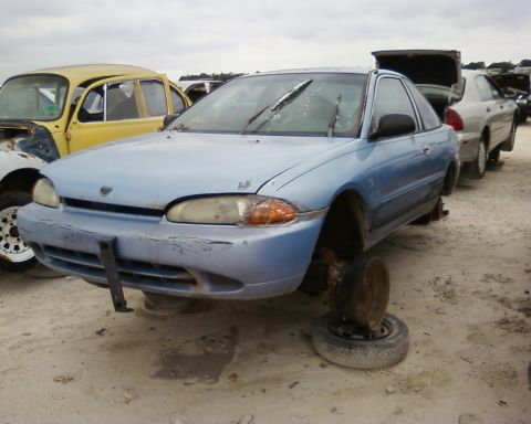 1991 Ford Festiva - Junkyard scene with a 1991 Ford Festiva missing wheels and other vehicles.