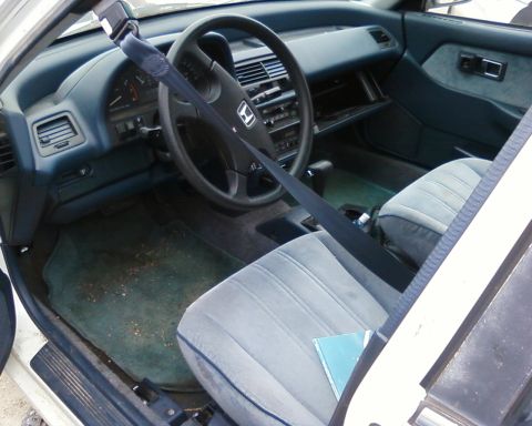 1991 Ford Festiva - The interior of a car shows worn seats and a cluttered dashboard, with a seatbelt prominently displayed.