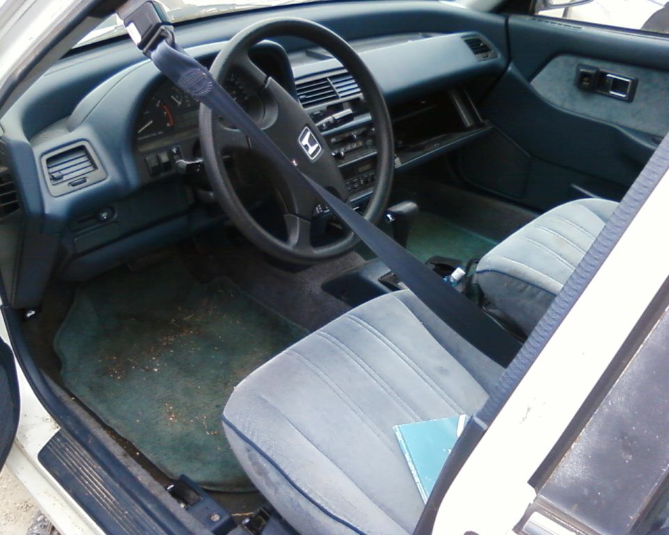 car interior with gray seats, dashboard, and steering wheel. Seatbelt is across the driver's seat