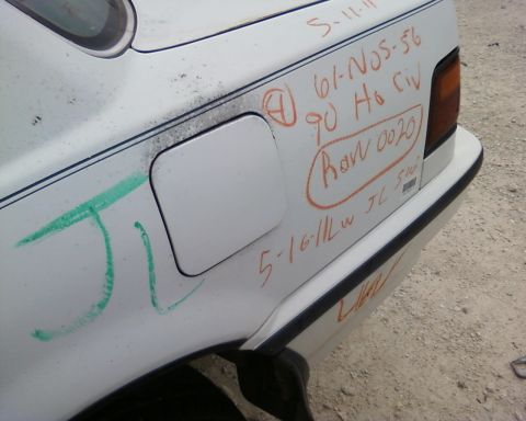 1991 Ford Festiva - Graffiti and handwritten notes cover the rear quarter panel of a white car, obscuring any identifying details.