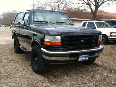 1996 Ford Bronco - A black Ford Bronco is parked in front of a house, with another white SUV visible behind it.