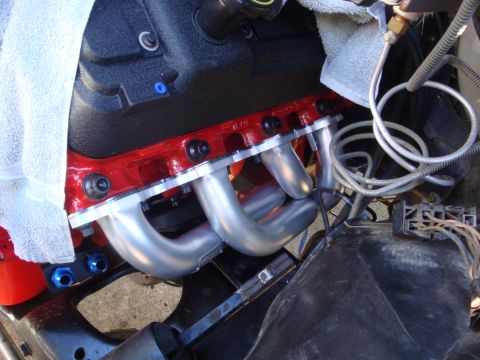 1989 Ford Bronco - Close-up view of an engine's exhaust manifold, showing the red painted block and silver pipes.