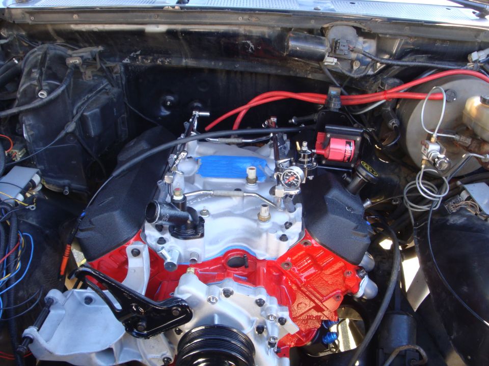 Engine bay with a red and silver V8 engine, red spark plug wires, and various hoses and components