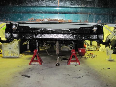 1979 Ford Bronco - The underside of a vehicle is supported by jack stands, with a teal body and black frame visible.
