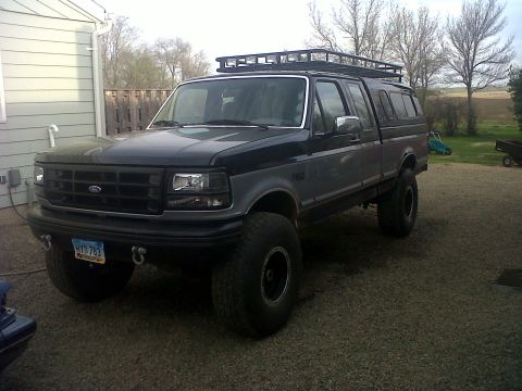 1994 Ford F-150 - This 1994 Ford F-150 pickup truck features a two-tone paint scheme, a roof rack, and a camper shell.