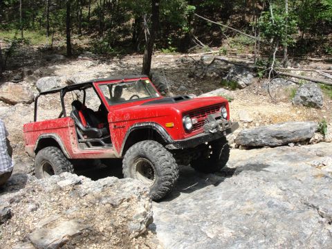 1967 Ford Mustang - Off-road SUV tackling a challenging rocky trail in a wooded area.