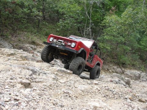 1967 Ford Mustang - A red Ford Bronco navigates a steep, rocky trail in a wooded area.