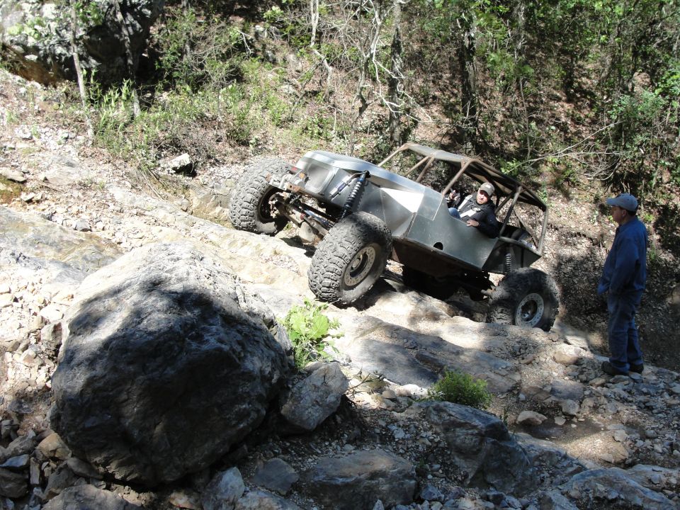 Off-road buggy with large tires climbing a rocky incline, person watching