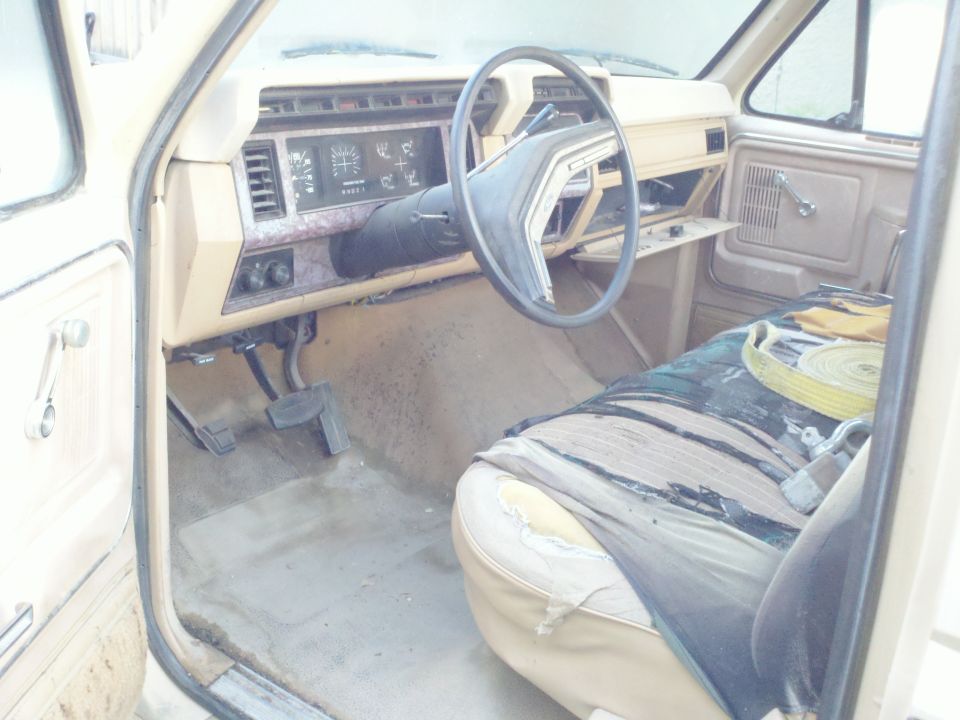 Tan interior of a truck with a torn seat cover and a steering wheel. The dashboard has gauges and vents