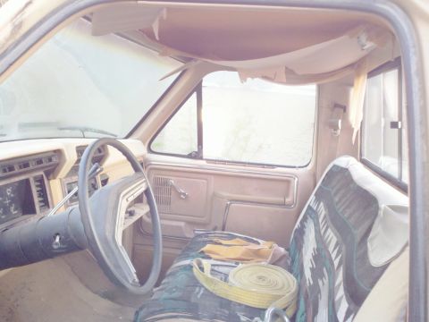 1985 Ford F-250 - The interior of a tan 1985 Ford F-250 pickup truck is visible, the dashboard, steering wheel, and a patterned seat cover.