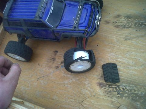 2011 Ford 427 - A blue remote control monster truck sits on a wooden surface with a detached tire nearby.