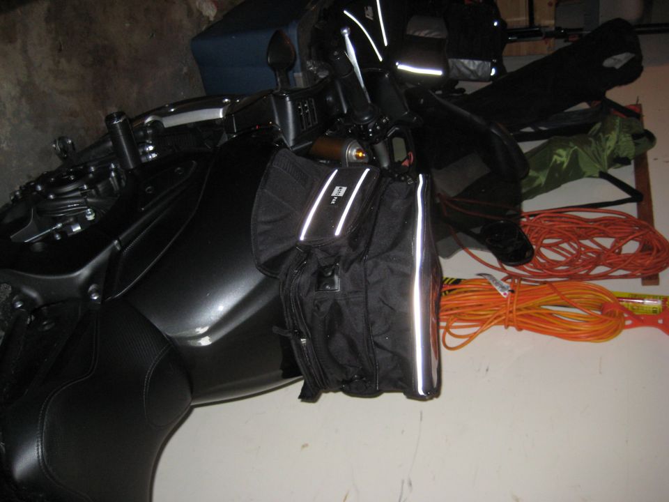 Motorcycle parked indoors with black saddlebags and reflective tape. Orange extension cords are nearby