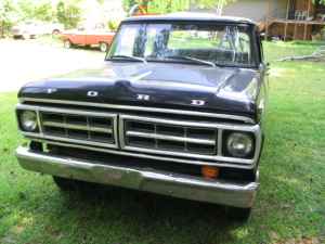 1995 Ford Bronco - Frontal view of a black 1970 Ford F-Series truck with a chrome grille and a dented hood, parked outdoors.