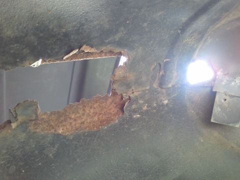1989 Ford Bronco - Detail of a rusted metal panel with a large hole, revealing the underlying structure.