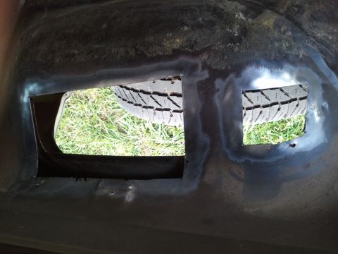 1989 Ford Bronco - Spare tire seen through cutouts in what appears to be a vehicle's undercarriage or cargo area.