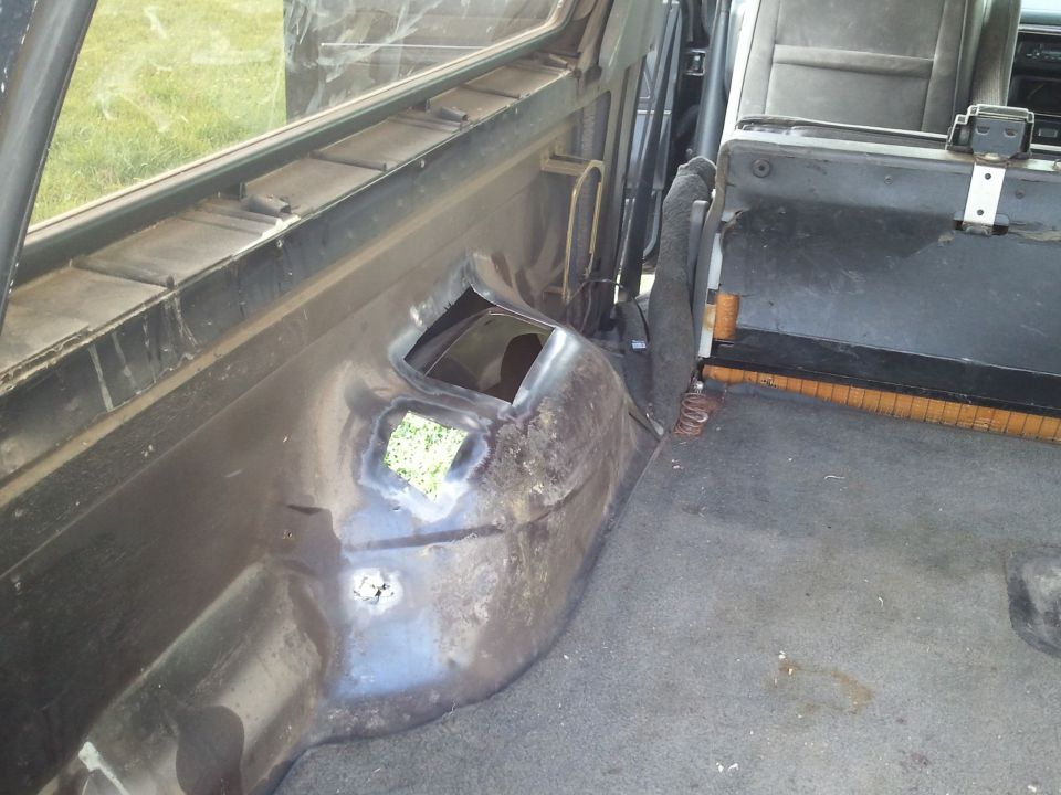 Interior rear wheel well area of a dark-colored SUV with rust and a hole showing grass outside