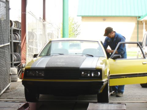 1979 Ford Mustang - A mechanic works on a yellow coupe, which appears to be a Mercury Capri.