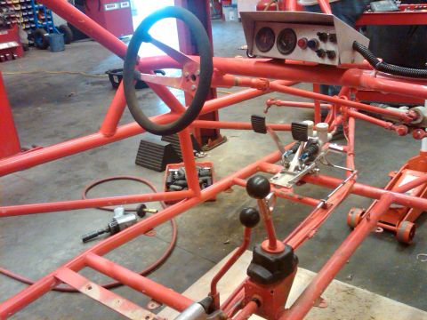 1995 Ford F-150 - The interior of a custom-built red tube frame chassis, a steering wheel, pedals, and dual gear shifters.