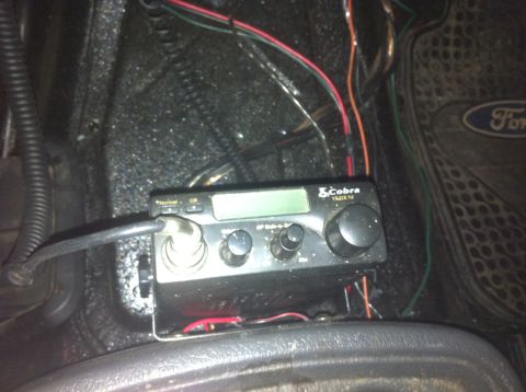 1990 Ford Bronco - A Cobra CB radio is installed in the interior of a vehicle, with wiring visible and a Ford-branded floor mat in the background.