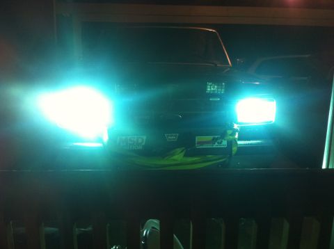 1990 Ford Bronco - The front of a 1990 Ford Bronco is illuminated by its bright headlights, with stickers visible on the grille.