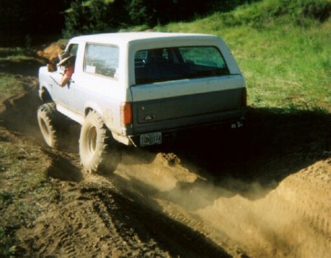1988 Ford Bronco - Ford Bronco navigates a dirt path off-road, kicking up dust from its tires.