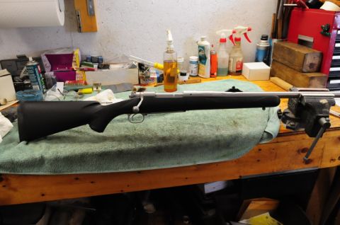 1991 Ford Bronco - Bolt-action rifle secured in a vise on a workbench, surrounded by various tools and cleaning supplies.