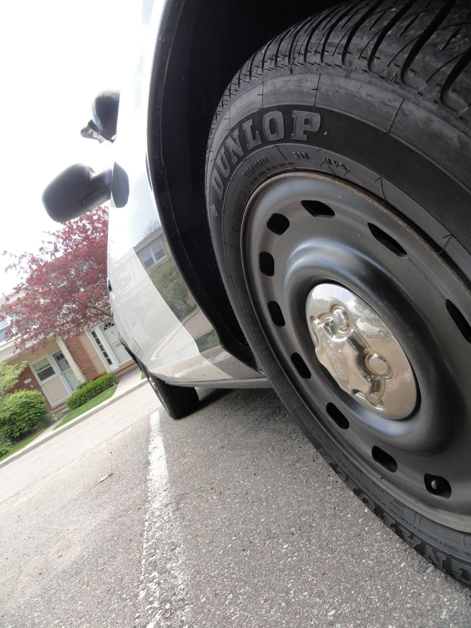 Close-up of a Dunlop tire and steel wheel with a chrome hubcap. Side mirror visible