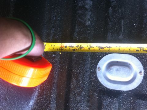 1990 Ford Bronco - A tape measure is used to measure an oval metal part located in the textured bed of a truck.