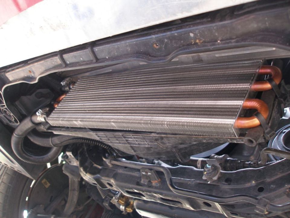 Underside view of an aftermarket oil cooler with copper lines, attached to a vehicle's frame
