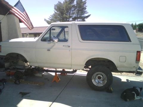 1995 Ford Bronco - A white Ford Bronco is parked outside a house, undergoing repairs with its front end removed.