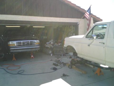 1995 Ford Bronco - Two Ford Broncos are undergoing maintenance in a garage, one black and one white.