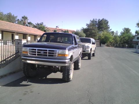 1995 Ford Bronco - Two SUVs are parked on a residential street under a clear blue sky.