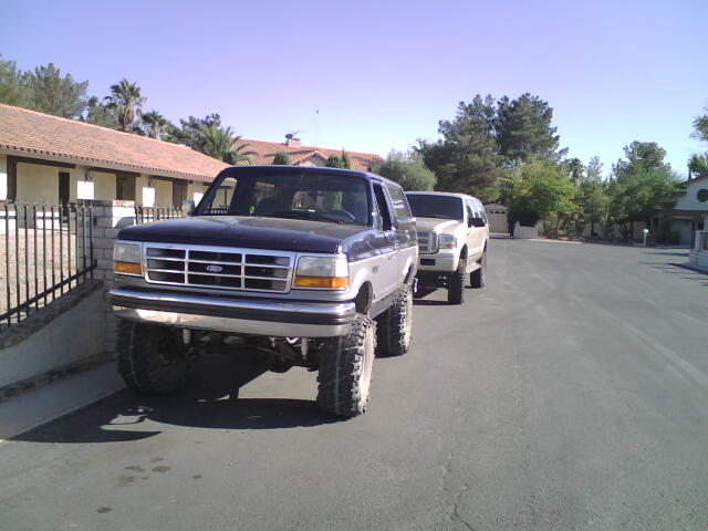 Dark blue and silver lifted Ford Bronco parked on street, another SUV behind it