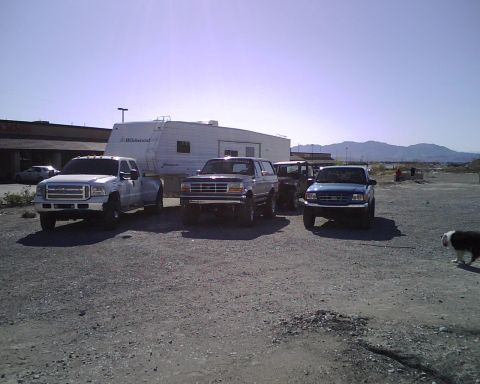 1995 Ford Bronco - Several Ford trucks and an SUV are parked together with a large trailer in a gravel lot.