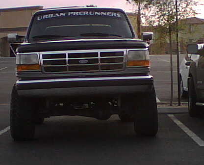 1995 Ford Bronco - A black Ford Bronco with a lifted suspension and "URBAN PRERUNNERS" text on the windshield is parked in a lot.