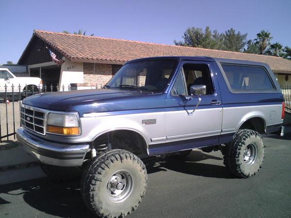 Blue and silver 1995 Ford Bronco, lifted with large tires, front 3/4 view