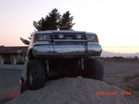 1995 Ford Bronco - Front view of a lifted Ford truck with large tires on a dirt mound at dusk.