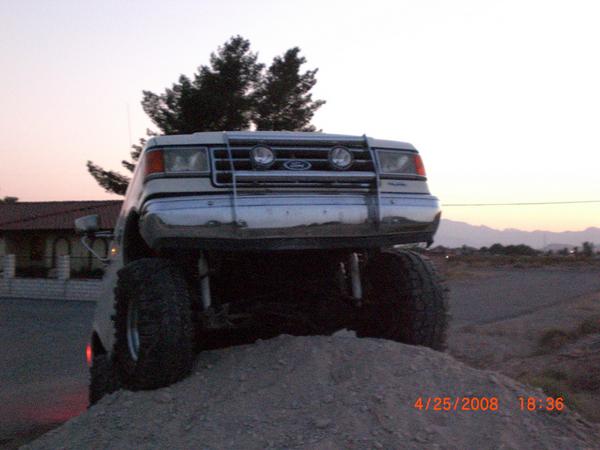 Lifted Ford truck with large tires on a dirt mound, front view