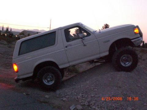 1995 Ford Bronco - A lifted white Ford Bronco navigates a dirt hill during a sunset.