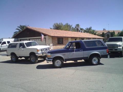 1995 Ford Bronco - Three SUVs, including two Ford Broncos and a Ford truck, are parked on a residential street.