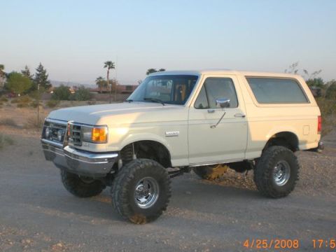 1995 Ford Bronco - This lifted Ford Bronco, likely from the late 1980s, sits on a dirt road under a clear sky.