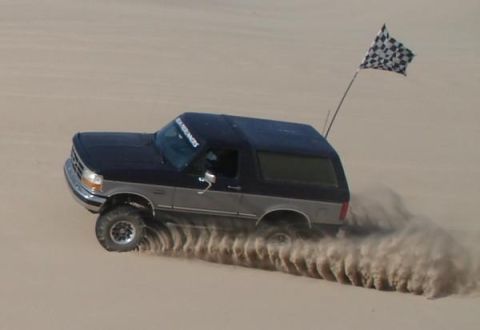 1995 Ford Bronco - Ford Bronco driving through sand dunes, kicking up a large plume of dust.