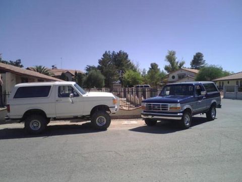 1995 Ford Bronco - Two Ford Broncos, a blue 1995 model and a white older model, are parked on a residential street.