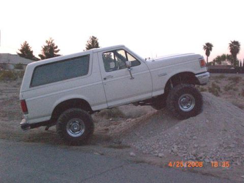 1995 Ford Bronco - White Ford Bronco with lifted suspension climbs a dirt mound during the day.