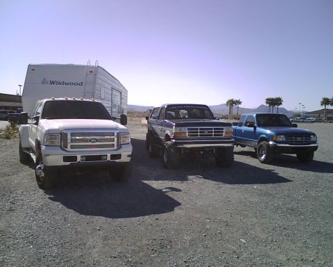 1995 Ford Bronco - A white dually truck, a lifted blue Bronco, and a blue Ford Ranger are parked outside.