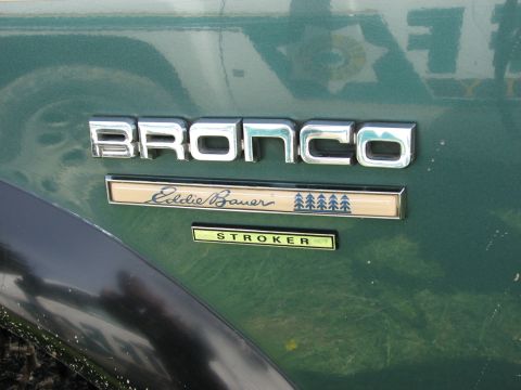 1990 Ford Bronco - Close-up of chrome BRONCO lettering and an Eddie Bauer script badge with pine-tree graphics on a dark green body panel, with a small custom…