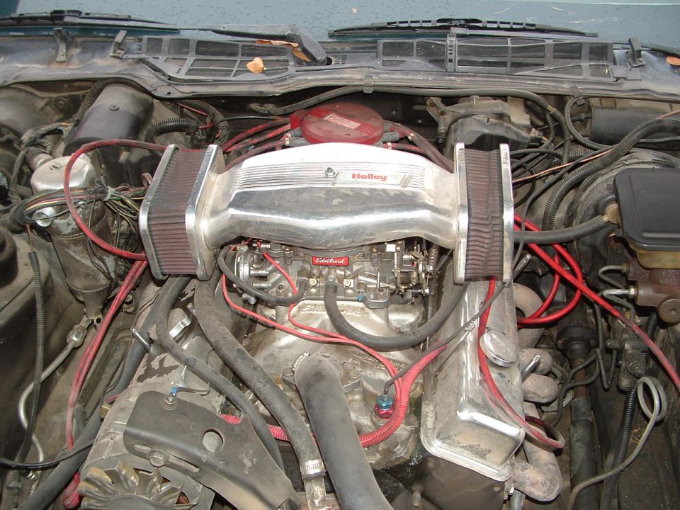 Engine bay with chrome Holley intake, Edelbrock carburetor, and red spark plug wires